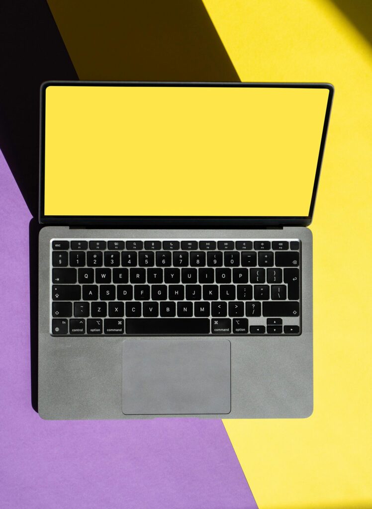 pexels-photo-16770280-16770280 Top view of a laptop with a yellow screen on a vibrant yellow and purple backdrop.